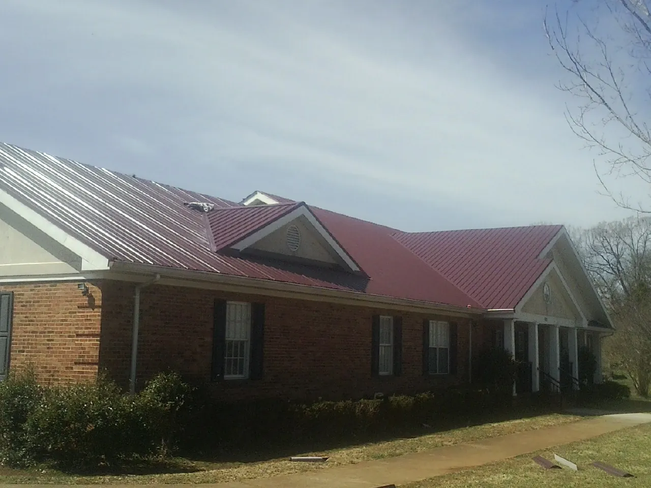 Red metal roof with gabled entries on a long brick building, from a Hail Damage Roof Repair job in Welaka