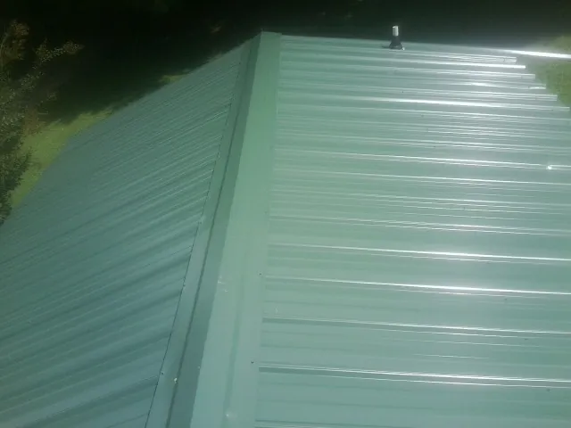 New green metal panels meeting at the ridge of a roof — Flat Roof Repair work by our crew in Welaka